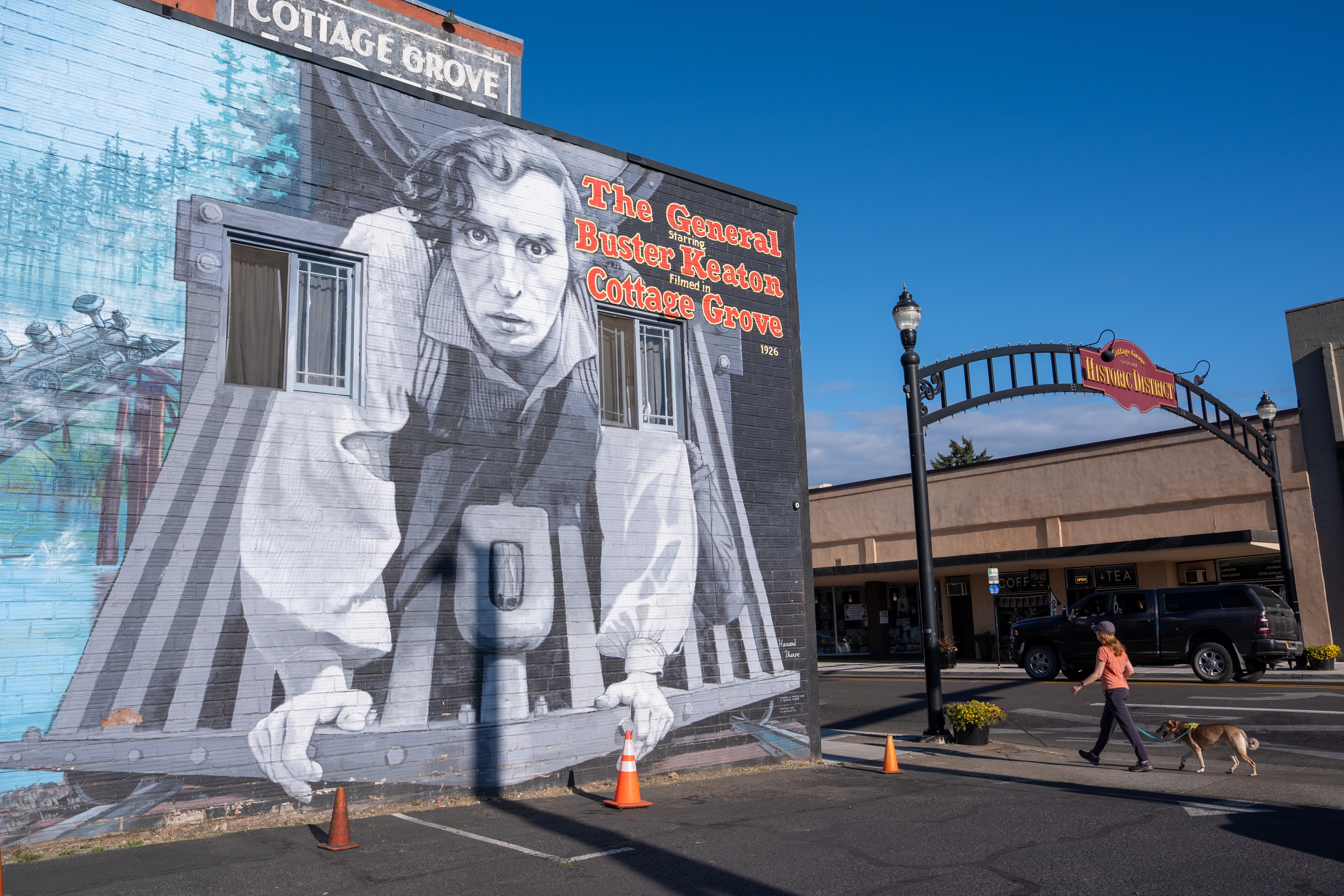 A woman walks her dog near a mural depicting Buster Keaton from his 1926 film, <em>The General,</em> in Cottage Grove, Ore. Fans gathered in the town to celebrate the film